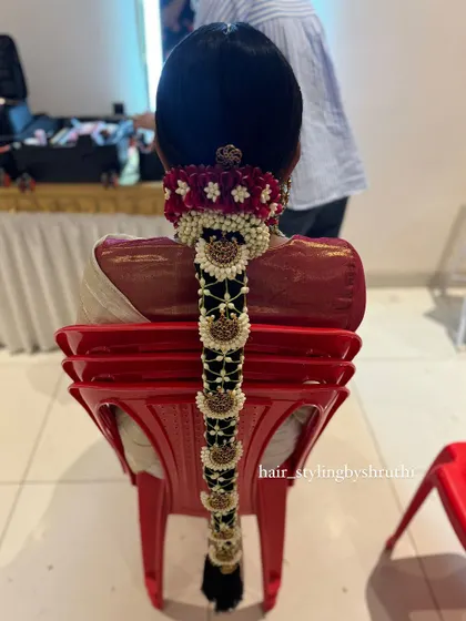A detailed look at a bridal poola jada, where the braid is decorated with fresh jasmine, red velvet flowers, and traditional temple jewelry. This style is a hallmark of South Indian bridal beauty.