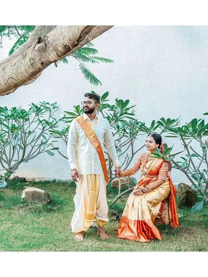 A sweet portrait of the couple in a garden, the groom standing while the bride sits, holding his hand.