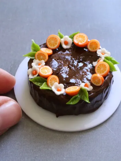 A close-up of a miniature chocolate fruit cake, adorned with tiny orange slices and flowers.