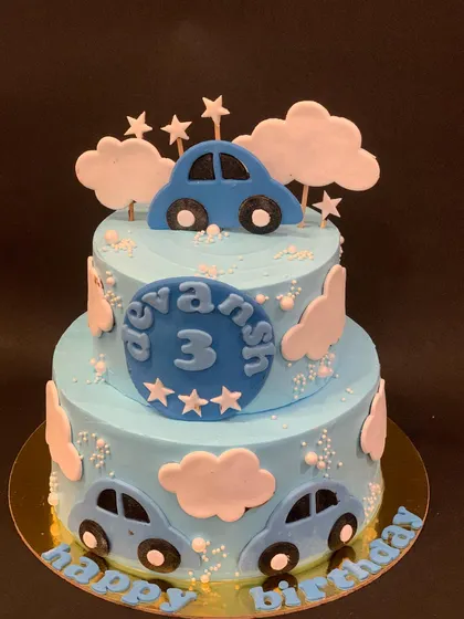 A two-tier blue car cake for a 3rd birthday. The design features cute cars and fluffy fondant clouds for a playful look.