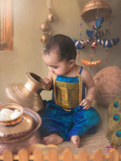 A little Radha curiously inspecting a brass pot, surrounded by rustic, traditional decor. Every detail in the setup is carefully chosen to build an authentic and artistic scene.