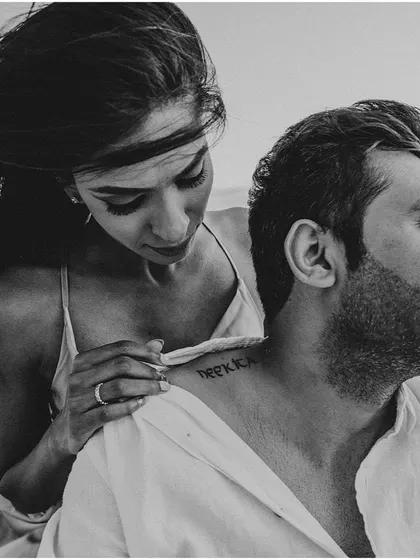A beautiful black and white shot focusing on a personal detail, the bride-to-be pointing to her partner's name tattooed on his neck.