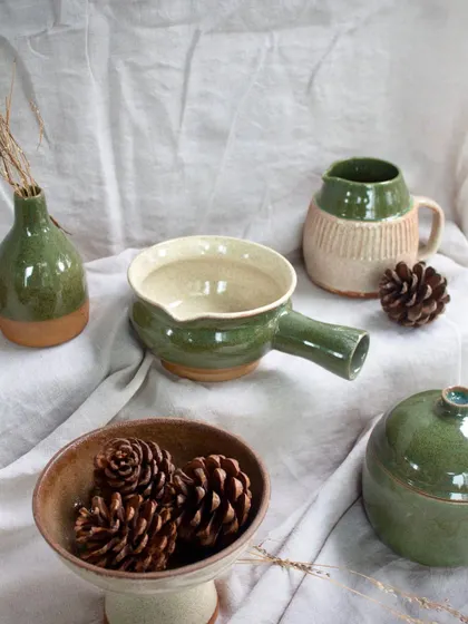 A lovely collection of student work in shades of green. This set includes a handled bowl, a mug, a lidded jar, and a small vase, all beautifully crafted and functional.