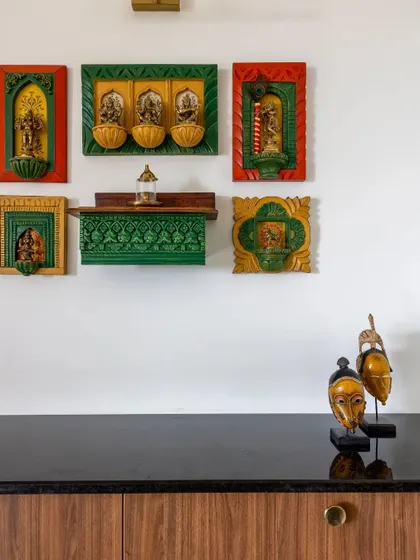 This charming puja area is combined with a crockery unit. The wall is adorned with colorful, framed decor of Hindu deities, creating a vibrant and spiritual corner in the home.