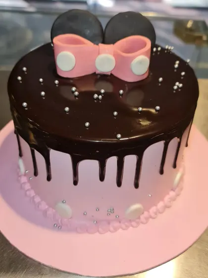 A classic Minnie Mouse theme cake, featuring a pink base, rich chocolate drip, and Minnie's signature pink bow and ears.