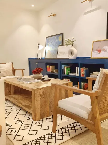 This view shows the full layout of the reading room. The custom blue built-in is balanced by neutral furniture, including a comfortable sofa and wood-and-cane armchairs. The geometric rug adds a modern touch and ties the space together.