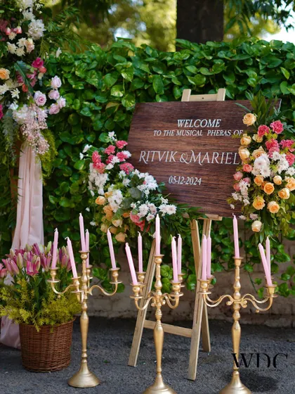 A beautiful wooden welcome board for the musical pheras, surrounded by an abundance of pastel flowers and elegant golden candelabras.