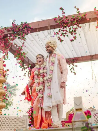 A beautiful shot of a multicultural couple at their wedding, standing under a vibrant floral mandap, representing the union of two souls.