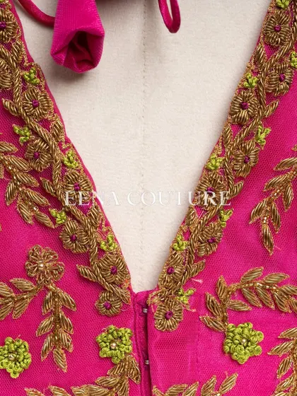 Grace in every detail. This pink net blouse features delicate leafy vines embroidered in gold and light green thread. The deep V-back and sheer sleeves add a touch of modern femininity.