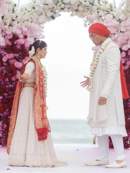 A candid moment of conversation between the bride and groom at the altar, surrounded by a magnificent floral arch. Their expressions tell a story of love and lighthearted connection during their beach wedding ceremony.