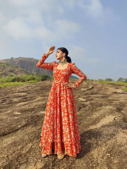 A dramatic shot of the orange floral Anarkali against a beautiful landscape.