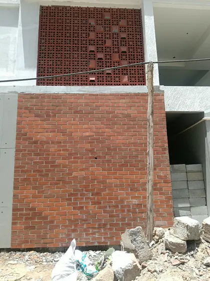This project shows a combination of classic red brickwork on the lower half and a decorative terracotta jali panel on the upper section. This mixed-material approach adds texture and visual interest to an exterior wall.