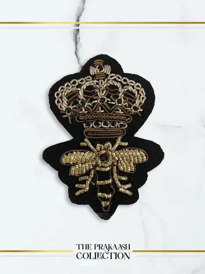 A detailed view of a hand-embroidered patch featuring a bee with a crown, crafted in gold thread on a black felt base. This is a popular motif for adding a touch of designer flair.