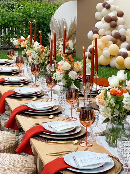 I can arrange a stunning backyard sundowner for a birthday celebration. This long table setup features warm terracotta tones, copper wine glasses, and beautiful floral centerpieces, creating a chic and inviting ambiance.
