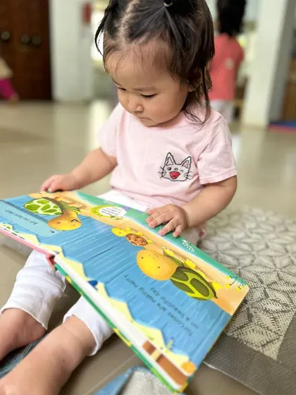 This toddler is exploring a colorful board book, learning to handle books and turn pages, which are important pre-reading skills.