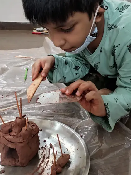 A student meticulously adds details to his clay creation. This close-up highlights the focus required for sculpting, an activity that strengthens both artistic skills and cognitive abilities.