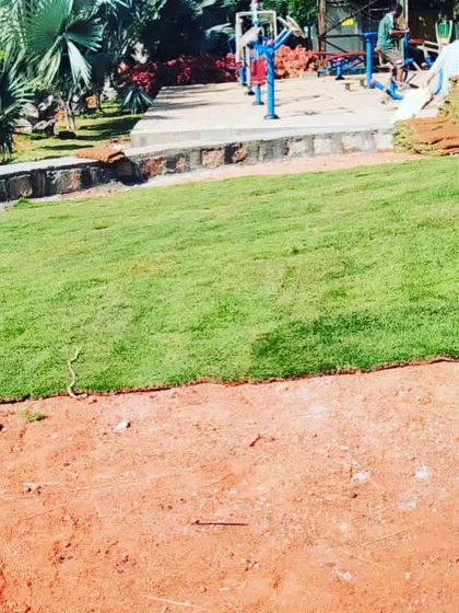 A park area being prepared for a new lawn, with rolls of grass ready for installation next to the red soil base.