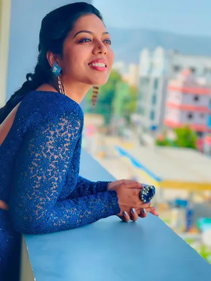 A happy and candid shot of a model in a blue sequin lehenga, looking out from a balcony.