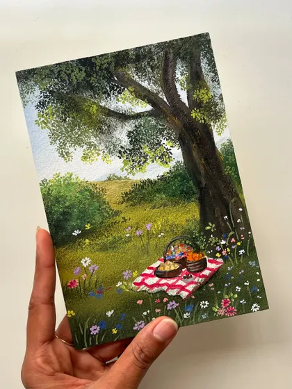 This piece captures the simple joy of a picnic in a wildflower meadow. I used gouache on paper to paint the checkered blanket, the basket of treats, and the peaceful landscape under a big tree.