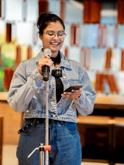 A poet shares her work on the "Wheel of Life" theme. The supportive atmosphere encourages personal and reflective performances.