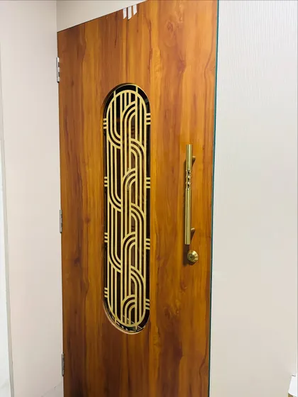 A close-up of a wooden safety door with an intricate gold-finished metal grill. The elegant handle and finish give it a premium, classic look.