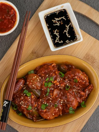 Saucy chilli momos presented in a bright yellow bowl. The contrast between the bowl and the dark, savory momos makes the dish look vibrant and full of flavor.