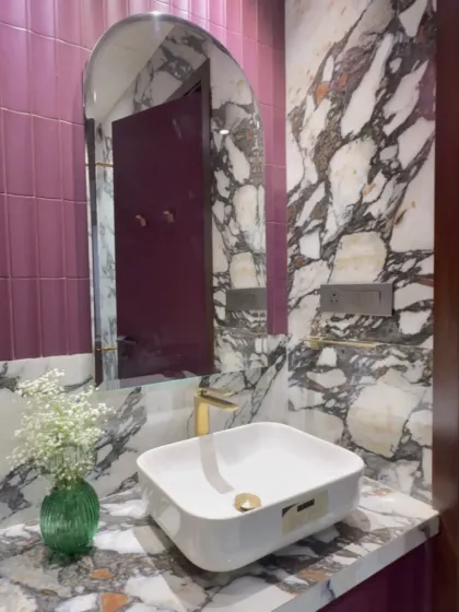 Color can completely transform a small space. Here, I paired bold magenta wall tiles with heavily veined black and white marble. The arched mirror softens the look, while the gold faucet adds a touch of warmth and luxury to this vibrant powder room design.