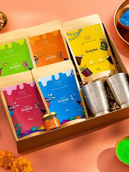 A festive flatlay for One Living's Holi-themed gift box. The box is styled with vibrant gulal, traditional glasses, and other festive elements to create a rich and celebratory image.