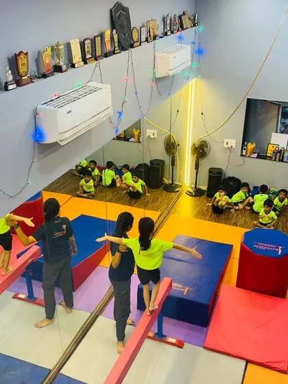 A bird's eye view of a typical gymnastics class at our Gorai studio. You can see children practicing on low balance beams with instructor assistance, while others wait their turn, showcasing our structured and supervised class environment.