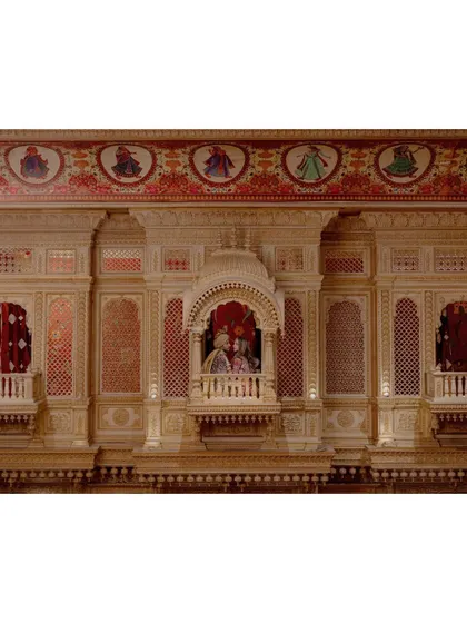 A wide shot capturing the magnificent, jharokha-style architecture of the wedding venue, with the couple seated like royalty in a balcony.