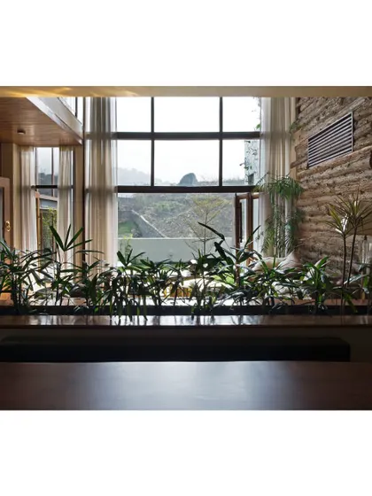 The dining area is designed to feel like a part of the landscape. A row of indoor plants acts as a natural screen, separating the space while still allowing views of the hills through the large windows, making every meal feel connected to nature.