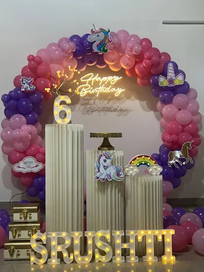 A magical unicorn themed sixth birthday party. The decoration features a circular balloon arch in pink and purple, unicorn cutouts, a neon sign, and a light-up number '6'.