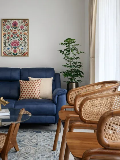 This image from the 'Malhar' project highlights the interplay of textures and colors, with a deep blue sofa, rattan chairs, and traditional Indian artwork. It's a space designed for a family of four, reflecting both comfort and character.