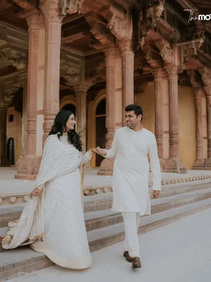 Walking hand-in-hand through the historic corridors of a Jaipur fort. The warm tones of the stone and the couple's serene white outfits create a beautiful, classic pre-wedding photograph that speaks of timeless love.