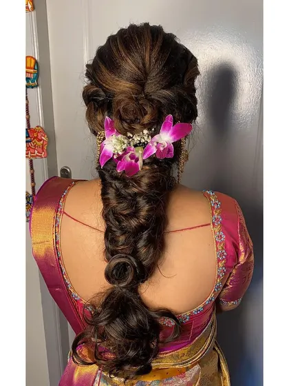 A beautiful messy fishtail braid with highlights, decorated with fresh orchids for a tropical and modern bridal look.
