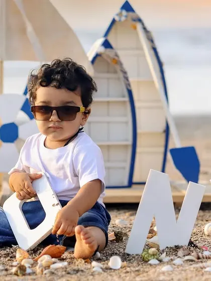 A cool one-year-old boy rocking sunglasses during his nautical-themed birthday shoot on the beach.