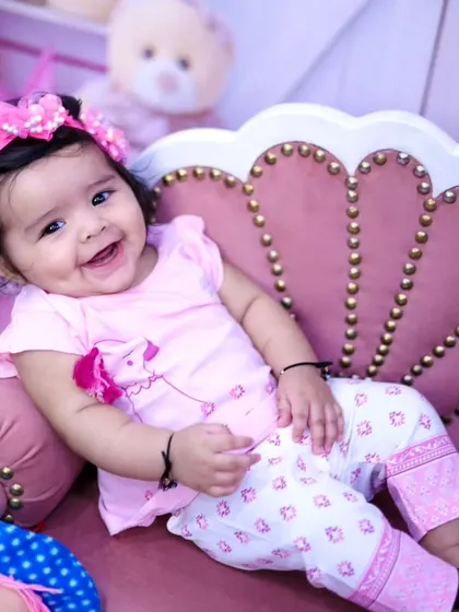 A beautiful, dimpled smile from a baby girl sitting on a pink shell-shaped couch.
