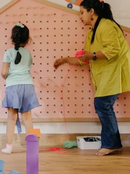 Collaboration and guidance are key in our Makerspace. An educator helps a child with a string art project on our pegboard wall, encouraging creativity and fine motor skills.