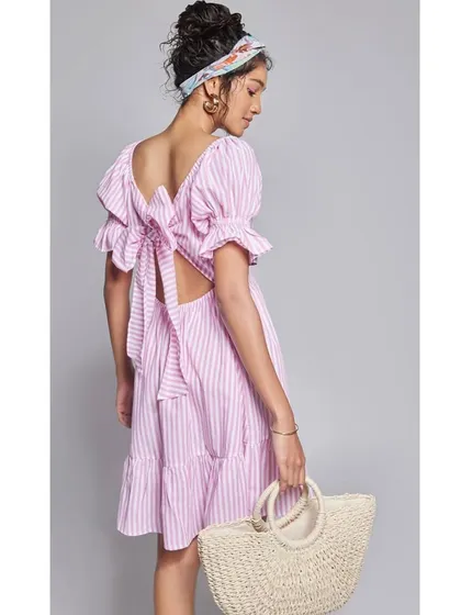 This image from a summer campaign features a pink and white striped dress with a cute back-tie detail, paired with a straw bag for the perfect vacation look.