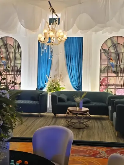 A sophisticated lounge area with deep teal sofas set against stained glass effect windows and elegant blue draping.