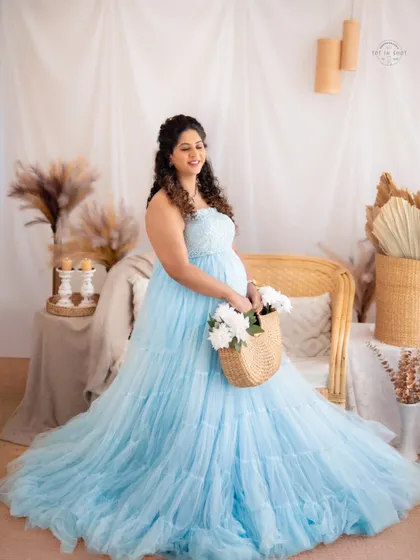 A charming portrait of an expecting mother in a blue tulle gown, holding a basket of white flowers in our rustic boho setting.