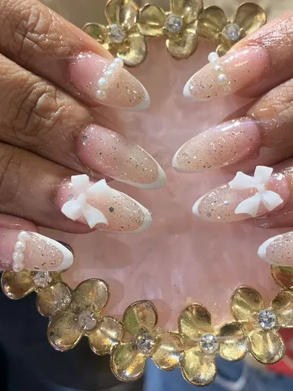 A variation of the French tip style, featuring a glittery ombre base, pearls, and 3D bow embellishments.
