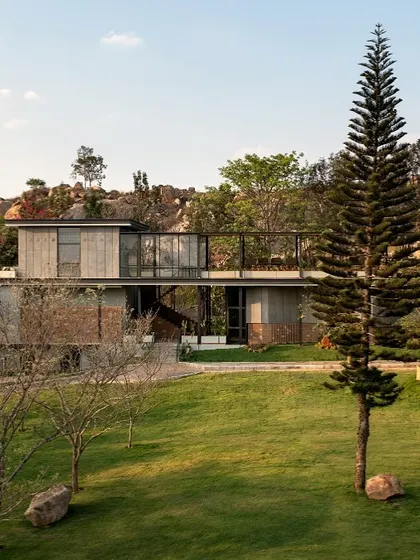 A daytime view of the structure's relationship with the rolling green lawns and rocky background. We work with the land, not against it, allowing the building to sit naturally within the existing contours and vegetation.