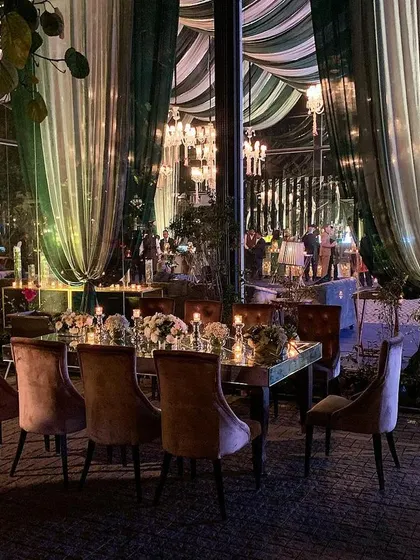 A view from the outside looking into a magnificent glass-walled venue. The green and white drapes create a beautiful reflection, offering a glimpse of the grandeur within and seamlessly connecting the indoor and outdoor spaces.