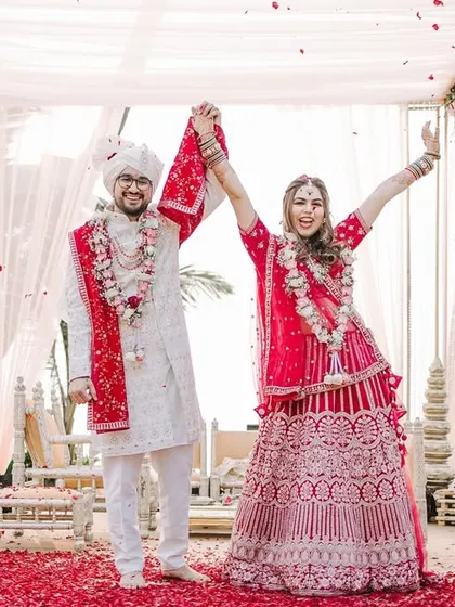 Pure joy and celebration after the Varmala. The couple raises their hands in triumph as they are showered with red rose petals.