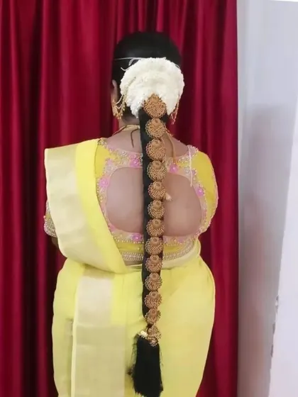 A traditional long braid adorned with evenly spaced, circular gold 'Jada Billas' and a fresh flower 'Gajra' at the base.