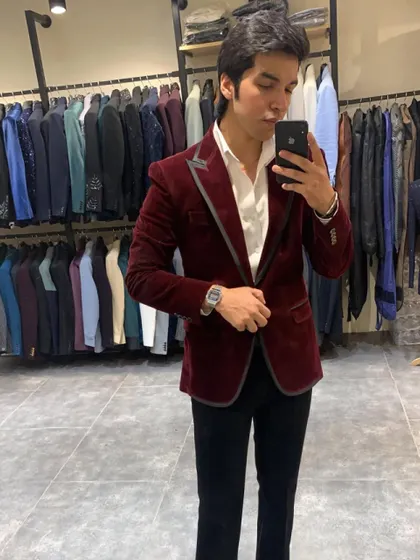 Another angle of the maroon velvet blazer, showing its tailored fit and the subtle sheen of the fabric. The grey piping on the lapel adds a modern, contrasting detail.