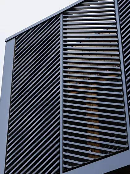 A close-up view of a building facade featuring louvered metal panels set at an angle. This architectural detail adds texture and a modern aesthetic while providing privacy and controlling sunlight.