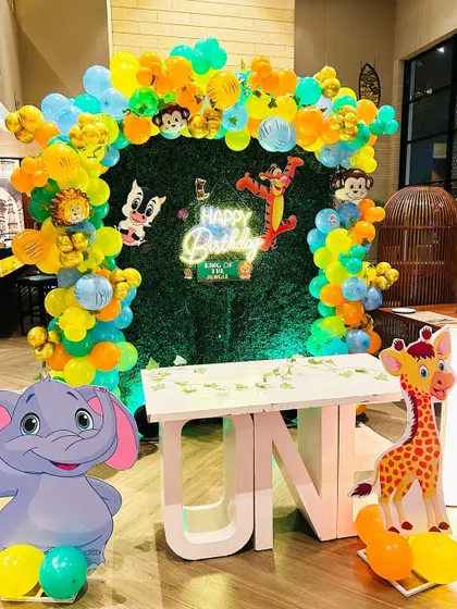 A jungle-themed first birthday party at Lemon Tree Hotel. The setup includes a "ONE" table, a green foliage backdrop, and various cute animal cutouts.