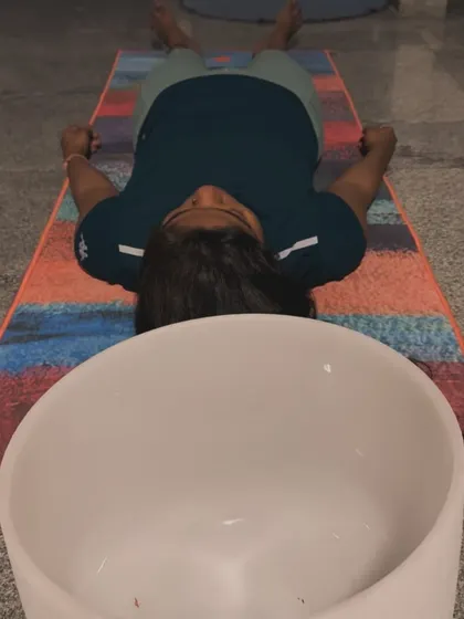 A participant lies in Savasana, fully immersed in the sound bath. The goal of these sessions is to facilitate a state of complete relaxation where the body's natural healing processes can take over.